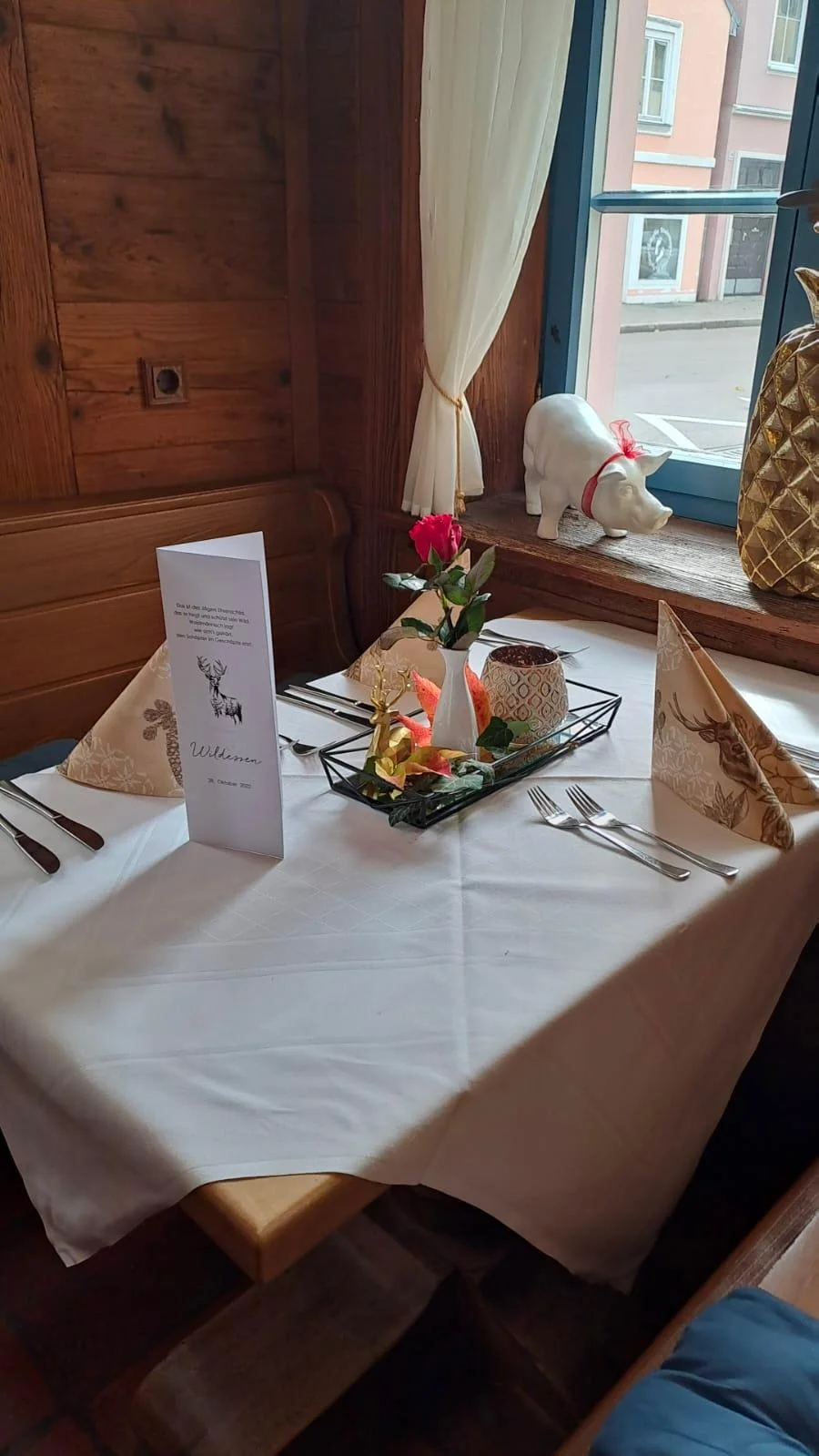 In einer holzgetäfelten Gaststube steht ein für drei Personen eingedeckter Tisch mit weißer Tischdecke.