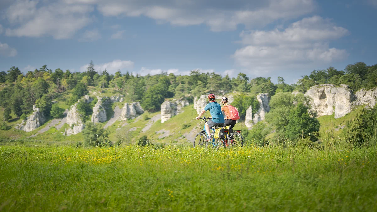 Radfahrer bei den 12 Apostel Solnhofen Zwei Personen fahren mit Fahrrädern auf einem grasbewachsenen Feld vor einer Felslandschaft.