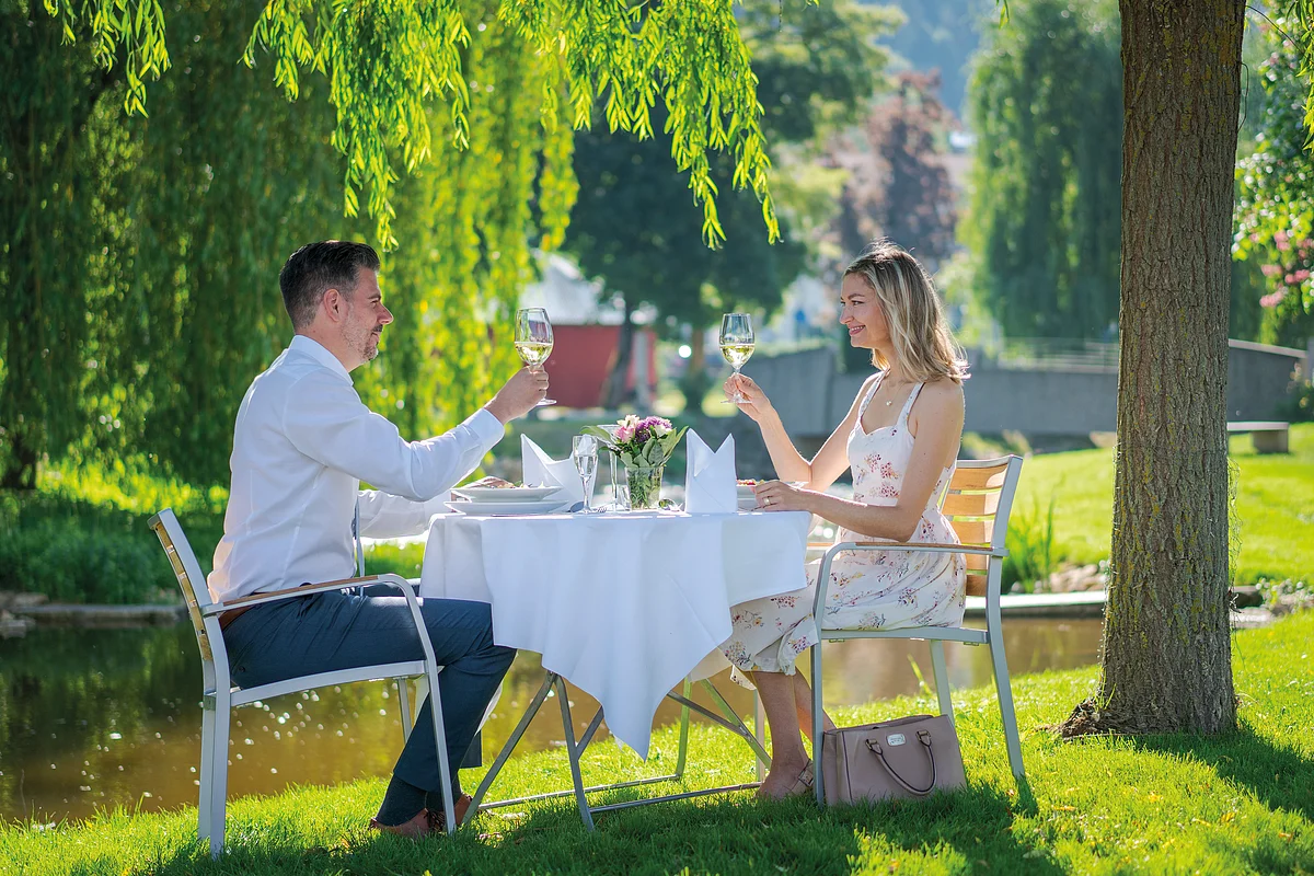 Stilvoll speisen im Sulzpark in Beilngries Zwei Personen sitzen an einem Tisch im Freien und stoßen mit Weingläsern an.