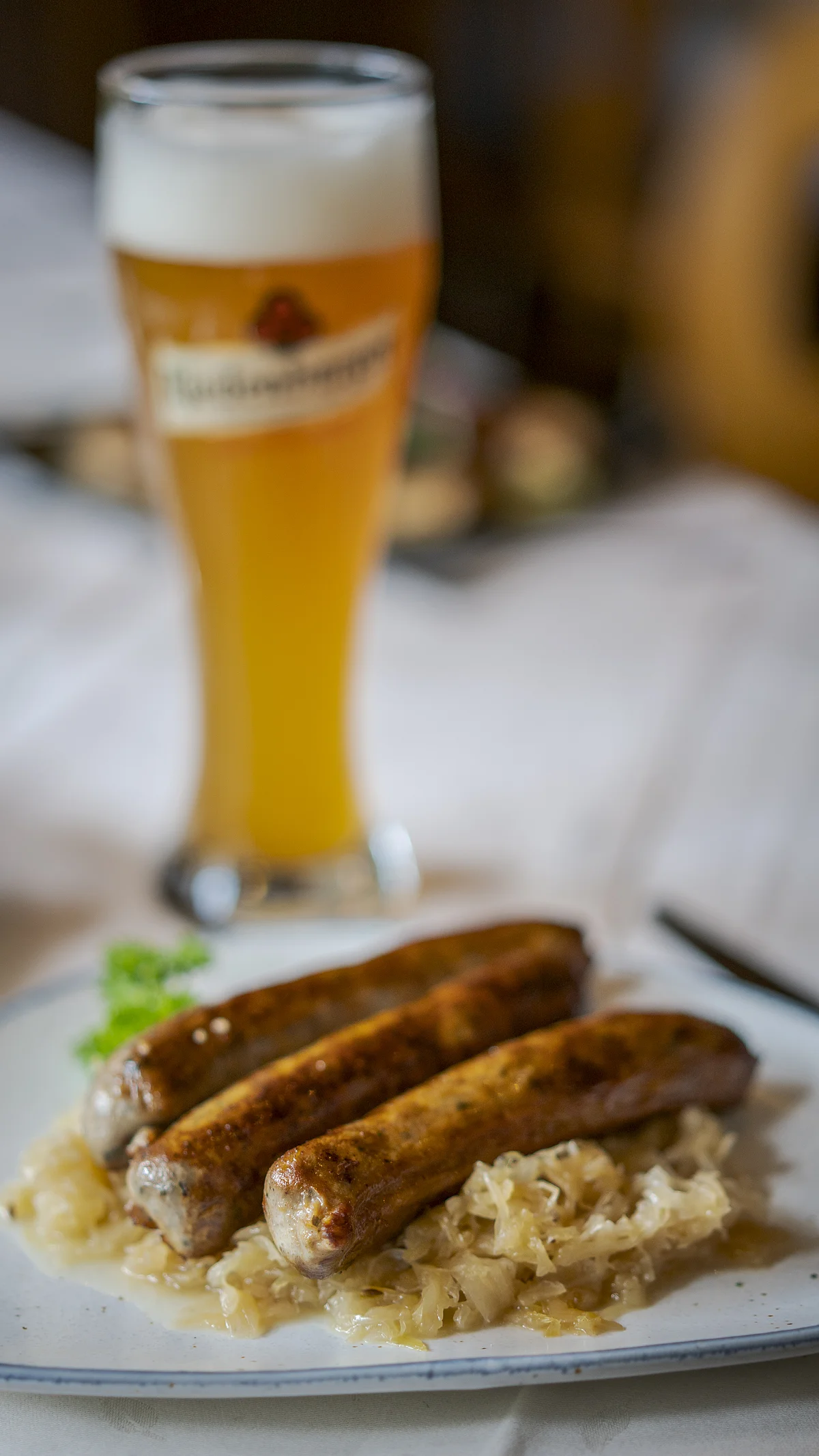 Bratwürste mit Kraut und Weißbier Drei Bratwürste auf Sauerkraut auf einem Teller, im Hintergrund ein Weizenglas mit Bier gefüllt.