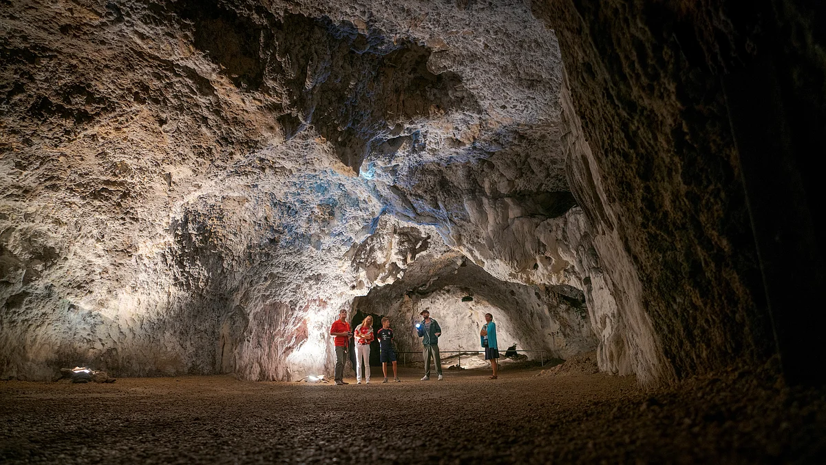Tropfsteinhöhle Schulerloch Fünf Personen stehen in einer großen, beleuchteten Höhle mit unregelmäßigen Felswänden und Boden aus Erde.