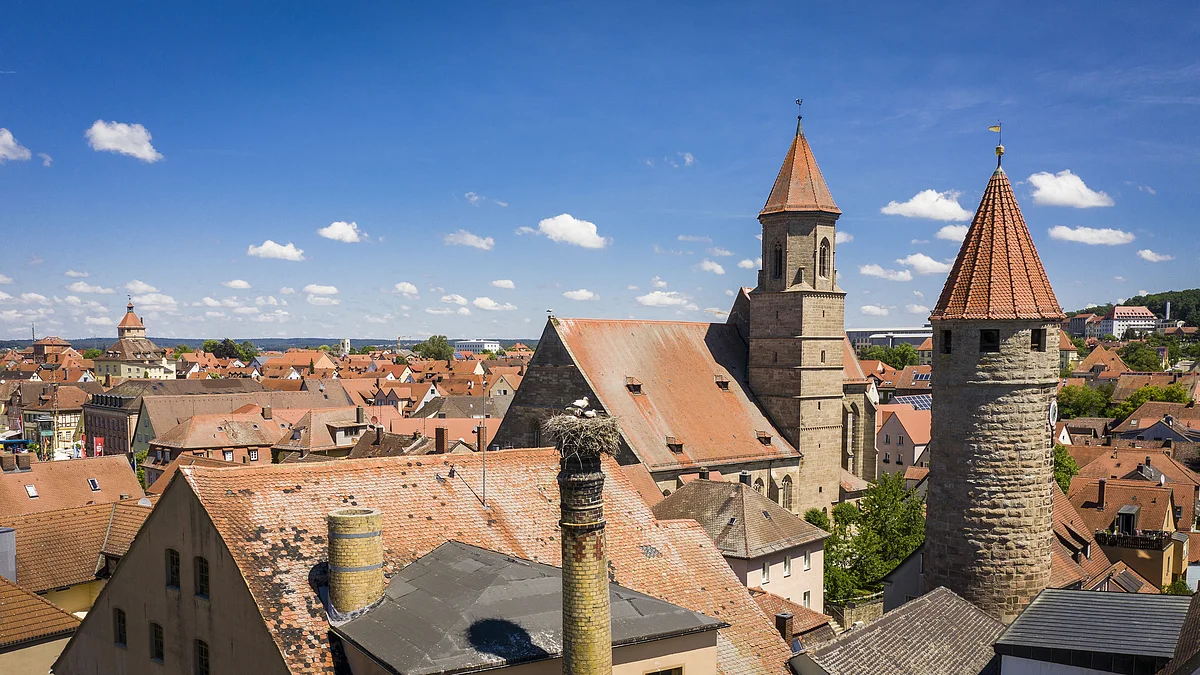 Gunzenhausen am Altmühlsee Stadtansicht mit roten Ziegeldächern, Kirchturm und rundem Steinturm unter blauem Himmel mit Wolken.